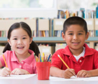 Kindergarten children sitting at desk and writing in classroom